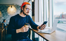 Serious Male Blogger In Spectacles For Provide Eyes Protection Watching Online Video Via Smartphone Application While Searching Content For Website, Caucasian Hipster Guy Reading News On Coffee Break