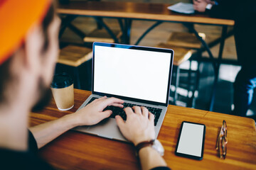 Cropped back view of millennial freelancer searching web information on mock up laptop computer with copy space area, skilled man using modern netbook and smartphone technology with blank screens