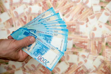 A man's hand holds Russian money worth two thousand rubles in close-up against the background of five thousand bills. The concept of Finance.