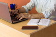 © Sausinbis - A Young man Working from Home on a laptop kept on a desk along with a cellphone, a dairy and a coffee mug.