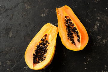 FFresh and tasty papaya cut in half on a black texture background. Copy of space