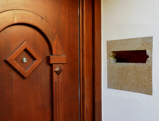 peephole and stone mail slot beside it on a beautiful warm brown pine entrance door of a house in daylight. depicting security and old traditional snail mail communications. home ownership concept.