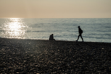 Silhouettes of people on the background of the sea and sunset. Solar path on the water. Small ripples ha surface of the water. Beach, a beach from a galois. Evening. Spring. Georgia.