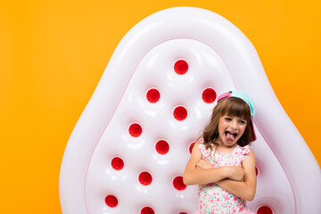 beautiful little girl in swinsuit holds a rubber mattress and smiles isolated on yellow and orange b