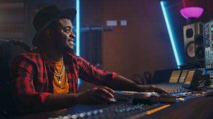 Fototapete - Stylish Audio Engineer / Producer Working in Music Recording Studio, Uses Mixing Board and Software to Create Modern Hit Song. Black Artist Musician Using Control Desk to Produce New Song.
