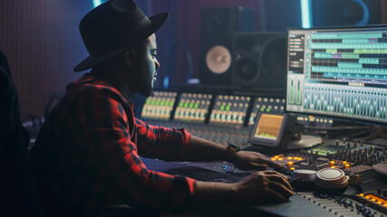 Wall Mural - Energetic Male Audio Engineer / Producer Working in Music Recording Studio, Mixing Tracks on Control Desk and Software to Create Hit Song Track. Artist Musician Enter His Studio at Sits at Workdesk