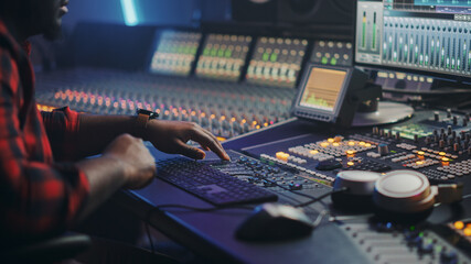 Fototapete - Energetic Male Audio Engineer / Producer Working in Music Recording Studio, Mixing Tracks on Control Desk and Software to Create Hit Song Track. Artist Musician Enter His Studio at Sits at Workdesk