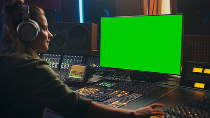 Fototapete - Stylish Female Audio Engineer / Producer Working in Music Record Studio, Uses Headphones, Green Screen Computer Display, Mixer Board, Control Desk to Create New Song. Creative Artist Musician.