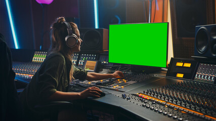 Fototapete - Stylish Female Audio Engineer / Producer Working in Music Record Studio, Uses Headphones, Green Screen Computer Display, Mixer Board, Control Desk to Create New Song. Creative Artist Musician.