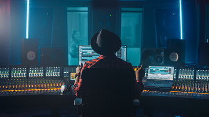 Fototapete - Producer, Audio Engineer Uses Control Desk for Recording New Album Track in Music Record Studio, in the Soundproof Room Musician, Artist, Performer Sings a Song from New Album. Back View 