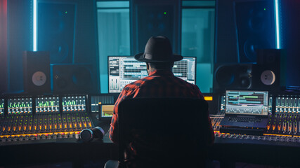 Fototapete - Stylish Artist, Musician, Audio Engineer, Producer Takes Place at His Control Desk in Music Record Studio, Uses Computer Screen show User Interface of DAW Software with Song Playing. Back View
