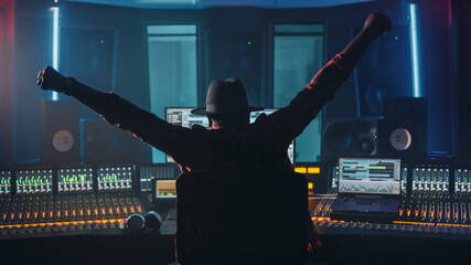 Fototapete - Artist, Musician, Audio Engineer, Producer in Music Record Studio, Uses Control Desk with Computer Screen showing Software UI with Song Playing. Celebrates Success with Raised Hands, Dances. Back View