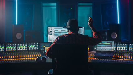 Wall Mural - Artist, Musician, Audio Engineer, Producer in Music Record Studio, Uses Control Desk with Computer Screen showing Software UI with Song Playing. Celebrates Success with Raised Hands, Dances. Back View