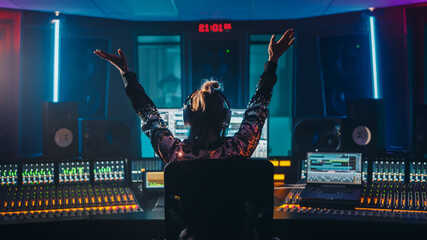 Fototapete - Artist, Musician, Audio Engineer, Producer in Music Record Studio, Uses Control Desk with Computer Screen showing Software UI with Song Playing. Celebrates Success with Raised Hands, Dances. Back View