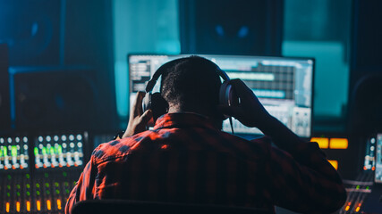 Fototapete - Stylish Artist, Musician, Audio Engineer, Producer Takes Place at His Control Desk in Music Record Studio, Uses Computer Screen show User Interface of DAW Software with Song Playing. Back View