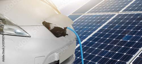 Close up of electric car with a connected charging cable on the background of solar panels