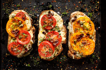 Wall Mural - Tomato toast grilled slices of sourdough bread with cheese and tomatoes sprinkled herbs on a black background, top view