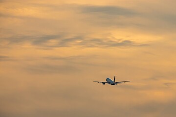 Beautiful dramatic gray cloud on orange sunset sky. Small silhouette of an airplane in the distance rising upward the clouds after takeoff. Air transport, natural colorful pattern sky background.