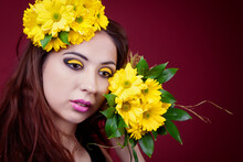 Portrait Of A Cute Girl With Bright Yellow Makeup And Yellow Chrysanthemums On A Red Background In The Studio.