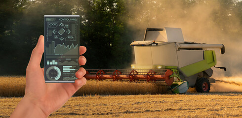 Fototapete - A farmer controls an autonomous combine harvester with a smartphone mobile application
