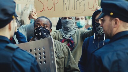 Young African American guy protester screaming and shouting at policemen at demonstration for human rights. USA protesters fighting and quarrelling with cops at protest against police violence.