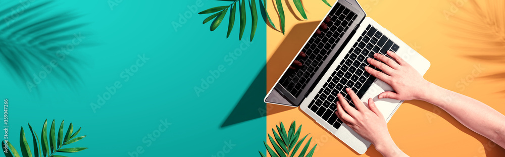 Person using a laptop computer with tropical leaves from above - obrazy, fototapety, plakaty 