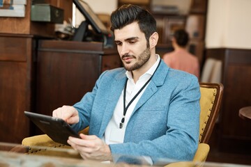 Canvas Print - Handsome young businessman sitting at cafe, using tablet computer. 