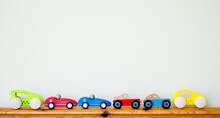 A Row Of Tiny Wooden Colorful  Toy Cars Lined Up Along A Child's Bed Headboard With Copy Space