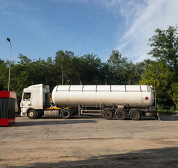 white tanker on the background of trees and the sky stands at the gas station