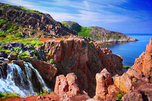 Waterfall In Teriberka, Murmansk Oblast, Kola Peninsula, Nortern Russia. Awesome Nature Scenery, Colorful Rocks, Green Moss And Barents Sea At The Background Of Blue Sky With Feather Clouds