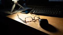 Glasses On A Desk With A Mouse, Keyboard, IPhone And Manfrotto Pixi Tripod. The Glasses Are Rayban Tortoiseshell And Are Lit From Above.