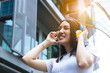 © Nutlegal - Young woman using headphone for listening nice music in city with building background with toothy smile, happiness, smile face. Asian pretty girl love listen music that make her relieve and relax