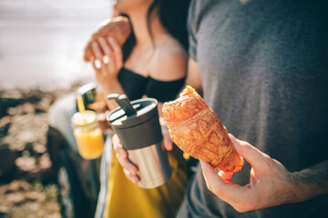 Wall Mural - They stopped for a snack. Close-up. croissants, thermo mug with coffee or tea and juice. Picnic near the water. Happy family on a road trip .