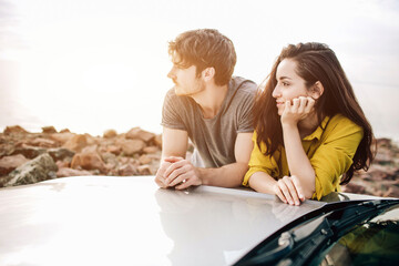 Wall Mural - young couple by a sports car parked on the beach. Romance and love in a car trip