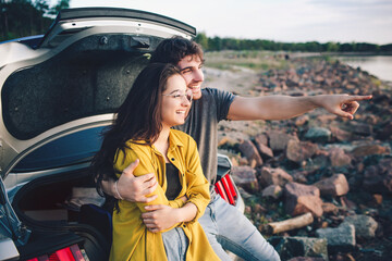 Wall Mural - Happy traveler couple sitting in car open trunk and watch the sunrise