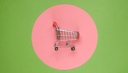 Shopping cart on green background with  pink pastel circle. Minimalistic shopping concept, shopaholic.