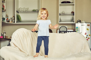 funny little girl standing on a couch. child playing at home.