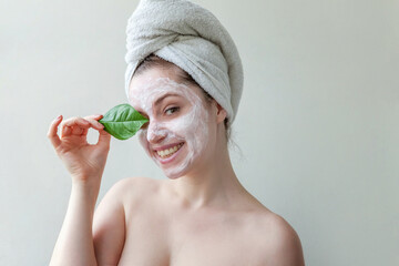 Minimal beauty portrait woman girl in towel on head applying white nourishing mask or creme on face, green leaf in hand isolated white background. Skincare cleansing eco organic cosmetic spa concept.