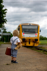 Wall Mural - Sweet toddler child with teddy bear, book and vintage suitcase waiting for the train on a train station