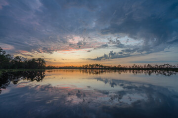 Sundown rose-pink light in raised bog. Konnu Suursoo (Korvemaa) wetland in Estonia. Sunset glow over marsh hollows.  Symmetry created by reflection of trees and colorful clouds in moorland lake.
