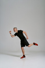 Wall Mural - Full length shot of middle aged muscular man in black sportswear looking aside while stretching his body during workout in studio over grey background