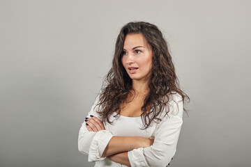 Standing and cross her arms on chest. Young attractive woman, dressed white blouse, with brown eyes, curly hair, yellow background