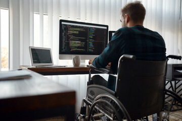 multitasking. back view of young caucasian male web developer in a wheelchair writing program code w