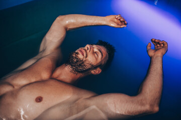 Handsome beard man floating in tank filled with dense salt water used in meditation, therapy, and alternative medicine.