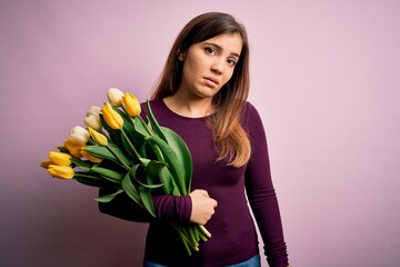 Poster - Young blonde woman holding romantic bouquet of yellow tulips flowers over pink background looking sleepy and tired, exhausted for fatigue and hangover, lazy eyes in the morning.