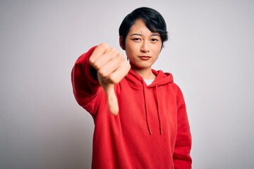 Poster - Young beautiful asian girl wearing casual sweatshirt with hoodie over white background looking unhappy and angry showing rejection and negative with thumbs down gesture. Bad expression.