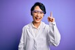 © Krakenimages.com - Young beautiful asian scientist girl wearing coat and glasses over purple background pointing finger up with successful idea. Exited and happy. Number one.