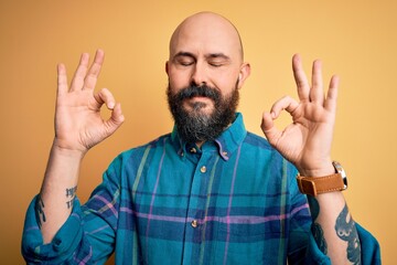 Wall Mural - Handsome bald man with beard wearing casual shirt standing over isolated yellow background relax and smiling with eyes closed doing meditation gesture with fingers. Yoga concept.