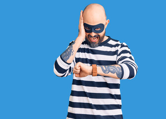 Poster - Young handsome man wearing burglar mask looking at the watch time worried, afraid of getting late