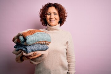 Poster - Middle age curly hair housework woman holding pile of clothes over isolated pink background with a happy face standing and smiling with a confident smile showing teeth